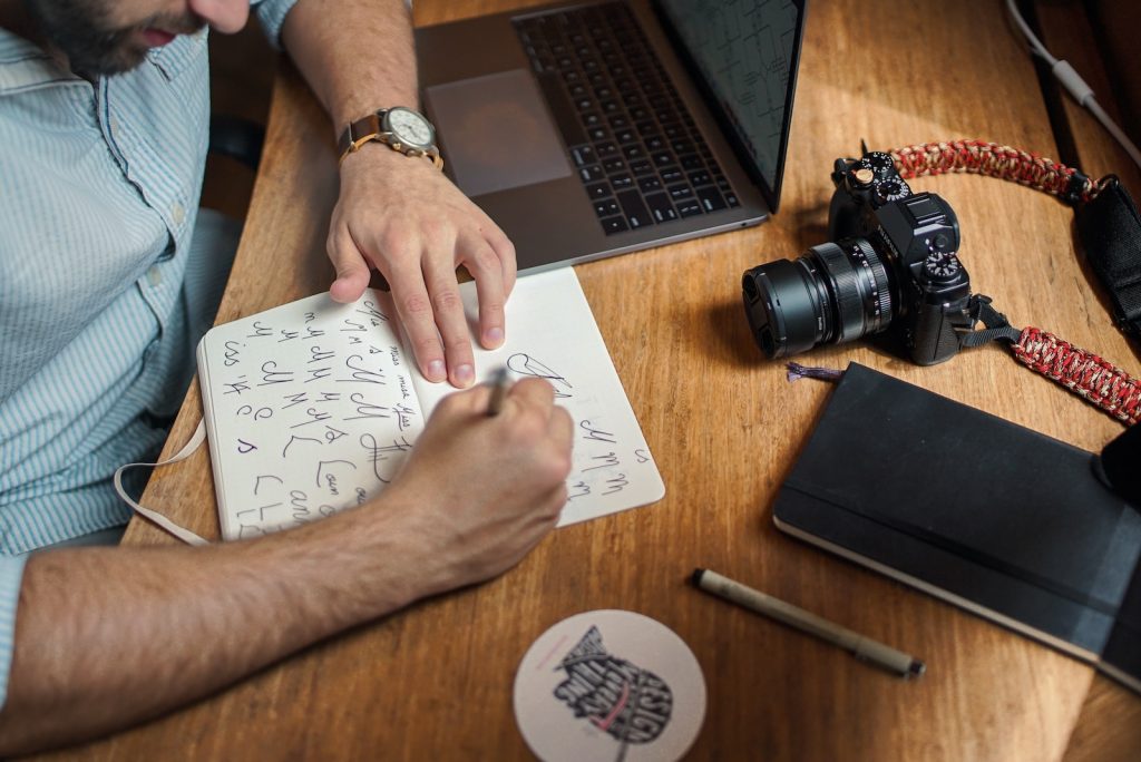 man writing on paper in front of DSLR branding